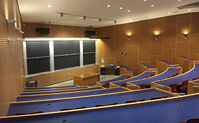 The front of a classroom, with arced tiers of desks facing a wall full of blackboards.