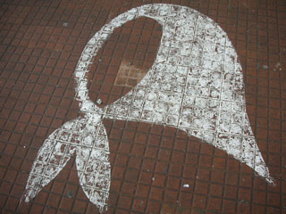 An image of a white shawl tied at the neck is superimposed on a red brick background.