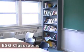 A photo of a classroom with a rectangular table with chairs around it. A chalkboard covers the wall at the front of the room.