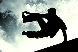 A photograph of the silhouette of a man vaulting over a wall set against a blue sky.