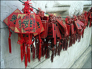 A few bunches of red cards with red strings and tassels hanging on a cord on a wall.