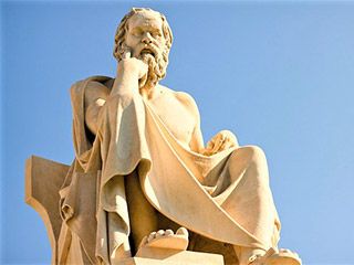 A marble statue of a seated, toga-wearing man with a furrowed brow and one hand resting on his chin.