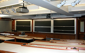 A view over several tiers of desks toward the classroom’s lectern area and blackboards.