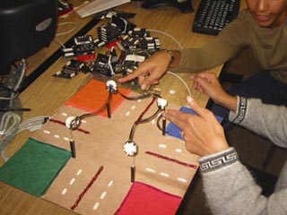 A photo of two students working on what looks like a minature four-way intersection.