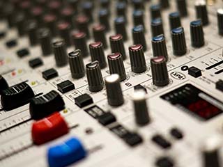 Closeup photo of slides and dials on an audio mixing console.