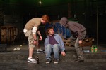 Two men look down on another man sitting on a city curb.