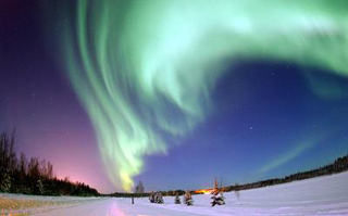 A green Aurora Borealis shimmers over snow-covered Alaskan fields.