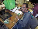 Photo of two students at a work table, one in the foreground preparing to solder a device into a circuit board.