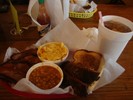 A meal consisting of baked beans, macaroni and cheese, tea, bread and barbecued meat is on a table. 